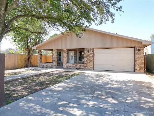 view of front of house featuring brick siding, driveway, an attached garage, and fence