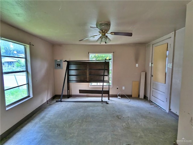 unfurnished room featuring ceiling fan, electric panel, concrete floors, and a healthy amount of sunlight