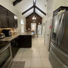 kitchen with kitchen peninsula, appliances with stainless steel finishes, dark brown cabinetry, light tile patterned floors, and vaulted ceiling with beams