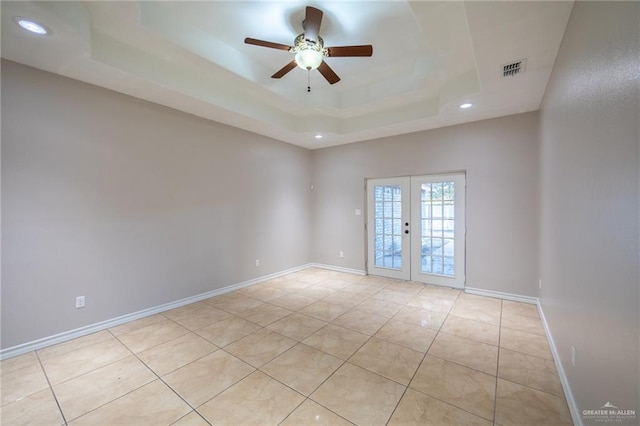 unfurnished room featuring a tray ceiling, ceiling fan, french doors, and light tile patterned flooring