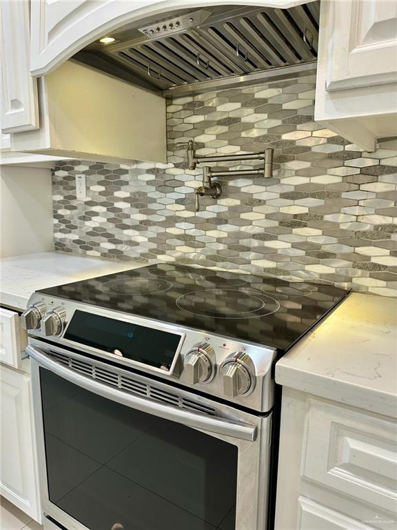2301 Mcleod Ave, Edinburg, TX 78539 - kitchen with stainless steel range with electric stovetop, tasteful backsplash, premium range hood, and white cabinets
