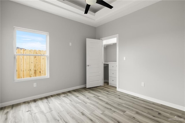 unfurnished bedroom with ceiling fan, a raised ceiling, and light hardwood / wood-style flooring