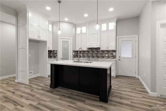 kitchen featuring pendant lighting, white cabinetry, an island with sink, sink, and light wood-type flooring