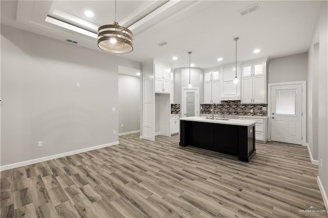 kitchen featuring white cabinetry, decorative light fixtures, light wood-type flooring, a tray ceiling, and an island with sink