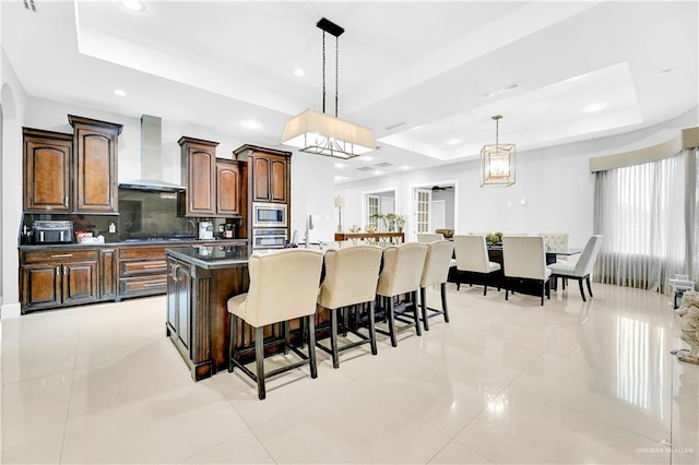 kitchen featuring appliances with stainless steel finishes, backsplash, a tray ceiling, wall chimney range hood, and pendant lighting