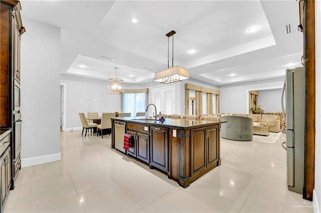 kitchen featuring stainless steel appliances, a raised ceiling, sink, a center island with sink, and hanging light fixtures