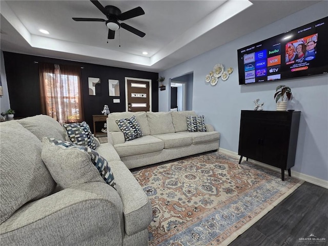 living room with wood-type flooring, a raised ceiling, and ceiling fan