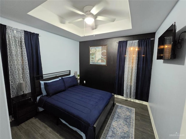 bedroom with a raised ceiling, dark wood-type flooring, and ceiling fan