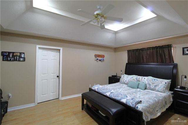 bedroom with a ceiling fan, light wood-type flooring, a raised ceiling, and baseboards