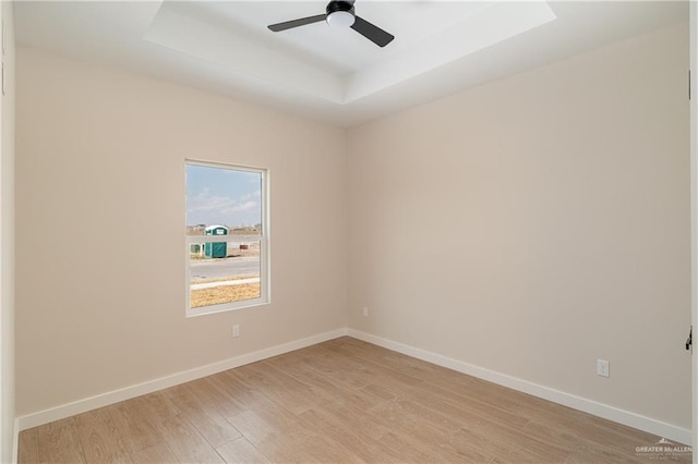 empty room with ceiling fan, light wood-type flooring, and a tray ceiling