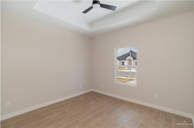 unfurnished room with a tray ceiling, ceiling fan, and light wood-type flooring