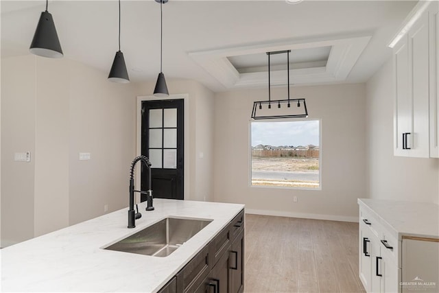 kitchen with a raised ceiling, white cabinetry, sink, and pendant lighting