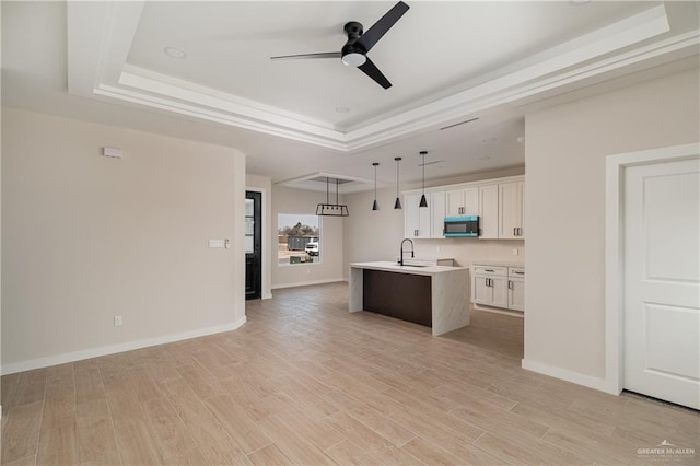 kitchen with sink, decorative light fixtures, a tray ceiling, an island with sink, and white cabinets