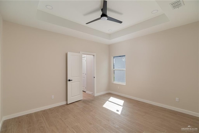 empty room with ceiling fan, a raised ceiling, and light wood-type flooring