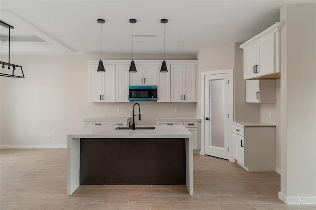 kitchen featuring a kitchen island with sink, sink, decorative light fixtures, and white cabinetry