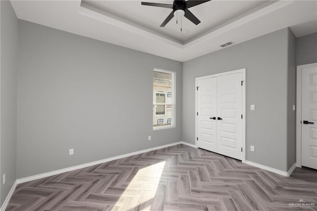 unfurnished bedroom with parquet flooring, a closet, ceiling fan, and a tray ceiling