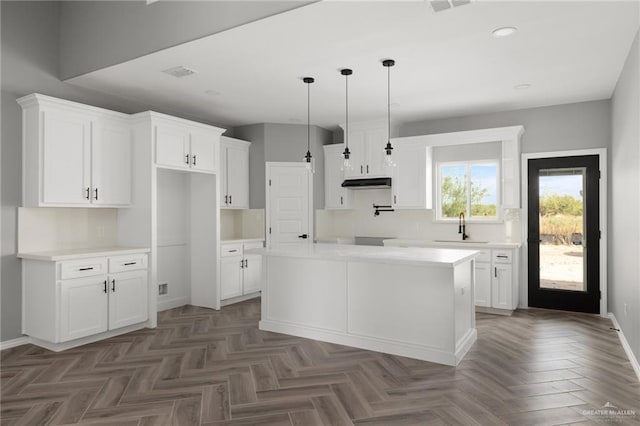 kitchen featuring a center island, dark parquet floors, sink, decorative light fixtures, and white cabinetry