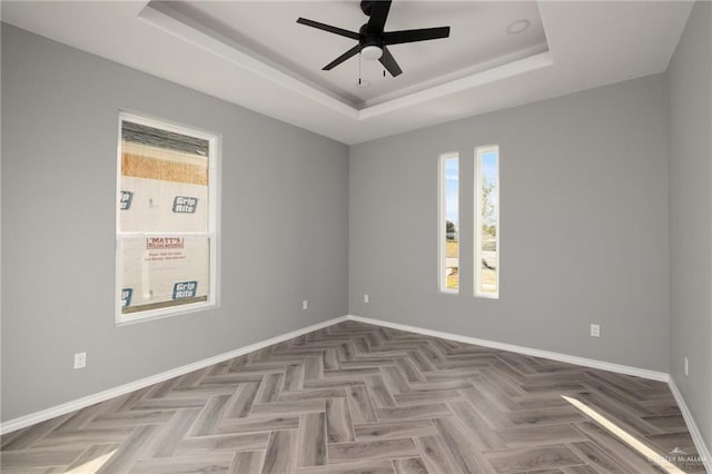 unfurnished room with a tray ceiling, ceiling fan, and parquet floors