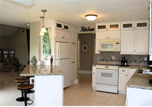 kitchen with light tile patterned flooring, a peninsula, white appliances, a breakfast bar, and white cabinetry