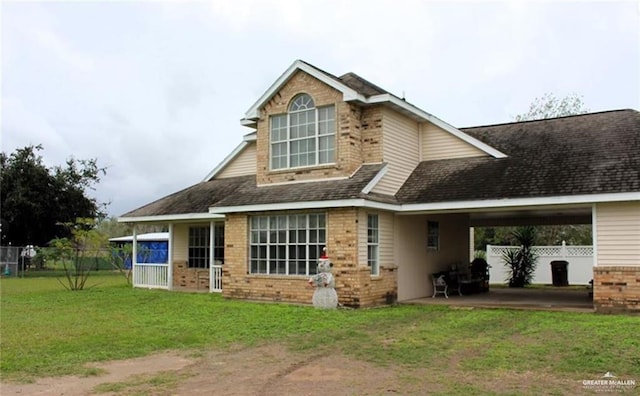 back of property with a shingled roof, brick siding, a yard, and fence