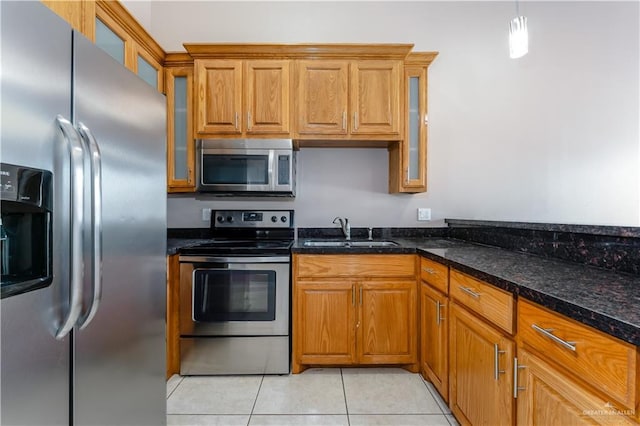 kitchen with light tile patterned floors, appliances with stainless steel finishes, brown cabinetry, and a sink