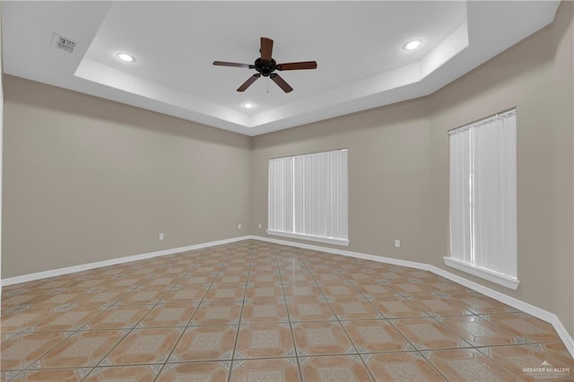 tiled spare room featuring ceiling fan and a tray ceiling