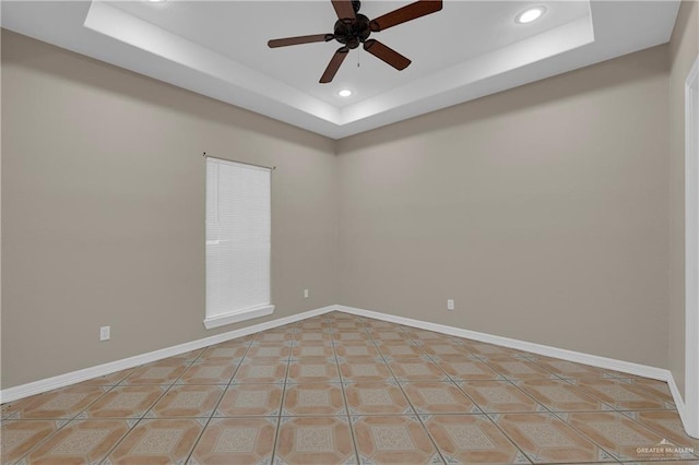 tiled empty room with ceiling fan and a tray ceiling