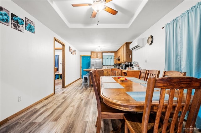 dining room with a wall mounted air conditioner, ceiling fan, a tray ceiling, and light hardwood / wood-style flooring