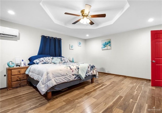 bedroom featuring hardwood / wood-style floors, ceiling fan, a wall unit AC, and a tray ceiling