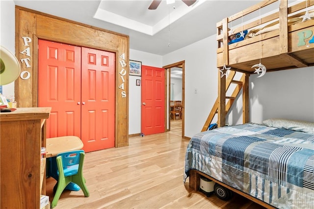 bedroom featuring ceiling fan, a closet, a raised ceiling, and light hardwood / wood-style flooring