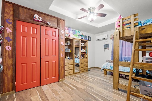 bedroom with ceiling fan, light hardwood / wood-style floors, a raised ceiling, and an AC wall unit