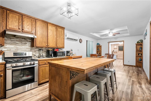 kitchen featuring stainless steel appliances, wood counters, a kitchen breakfast bar, a wall unit AC, and light hardwood / wood-style floors