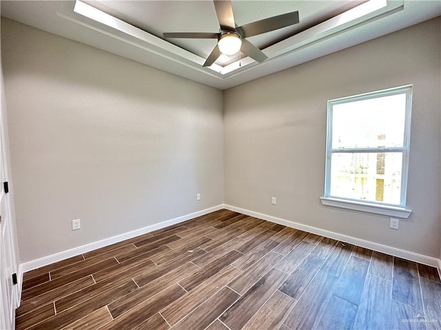 empty room with a raised ceiling, ceiling fan, and dark wood-type flooring