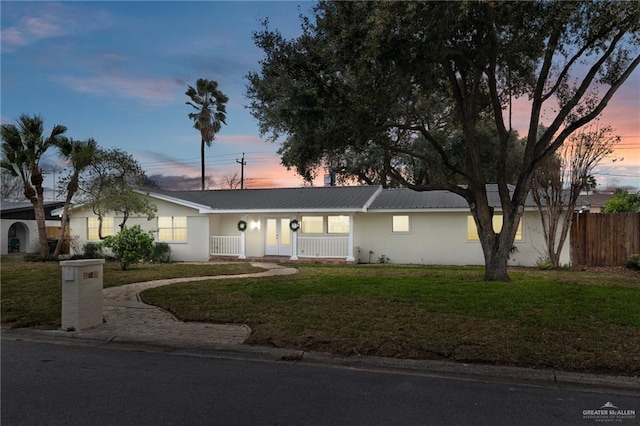 ranch-style house featuring metal roof, covered porch, fence, stucco siding, and a front lawn