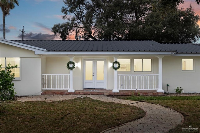 exterior entry at dusk featuring a porch, french doors, metal roof, and stucco siding