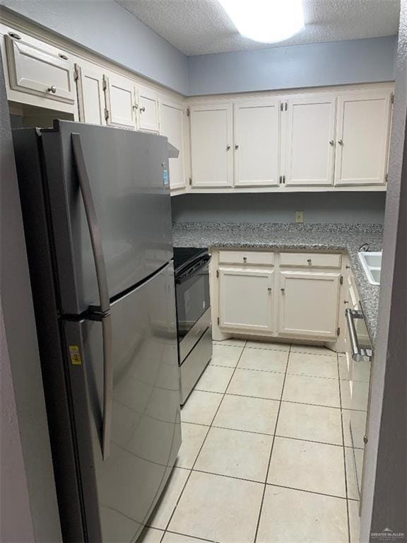 704 Kerry Ln, Mcallen, TX 78504 - kitchen with freestanding refrigerator, electric stove, a textured ceiling, white cabinets, and light tile patterned floors