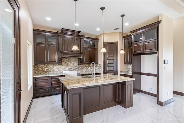 kitchen with hanging light fixtures, dark brown cabinetry, sink, and a kitchen island with sink