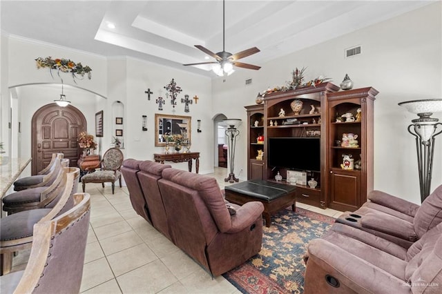 tiled living room with a tray ceiling, ceiling fan, crown molding, and a towering ceiling