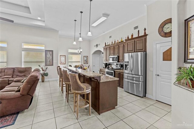 kitchen with light stone countertops, a kitchen breakfast bar, stainless steel appliances, a center island, and hanging light fixtures