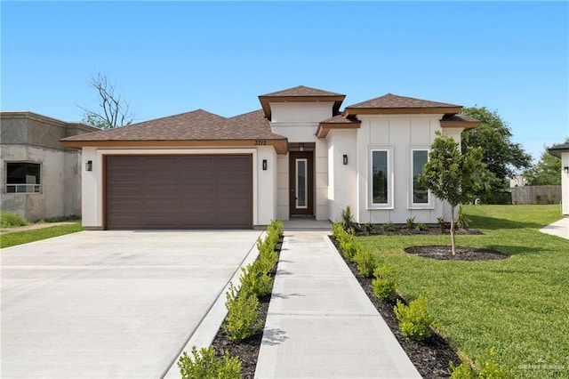 prairie-style home featuring an attached garage, stucco siding, concrete driveway, a front lawn, and roof with shingles