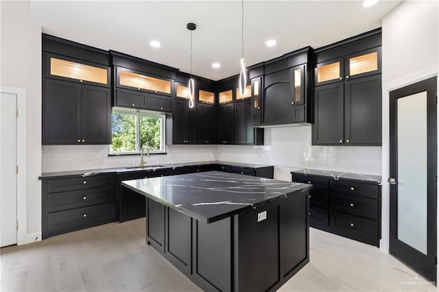 kitchen featuring a sink, backsplash, a center island, and dark cabinets