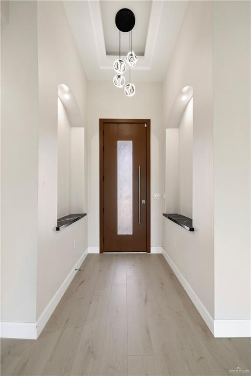 foyer entrance with baseboards, a raised ceiling, and light wood-type flooring