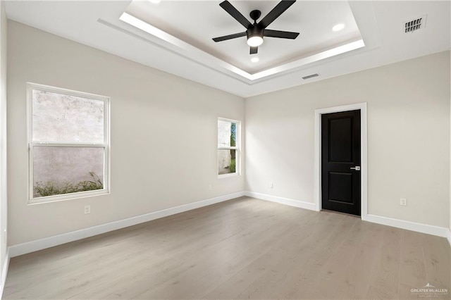 empty room featuring a raised ceiling, a ceiling fan, visible vents, and light wood-style floors