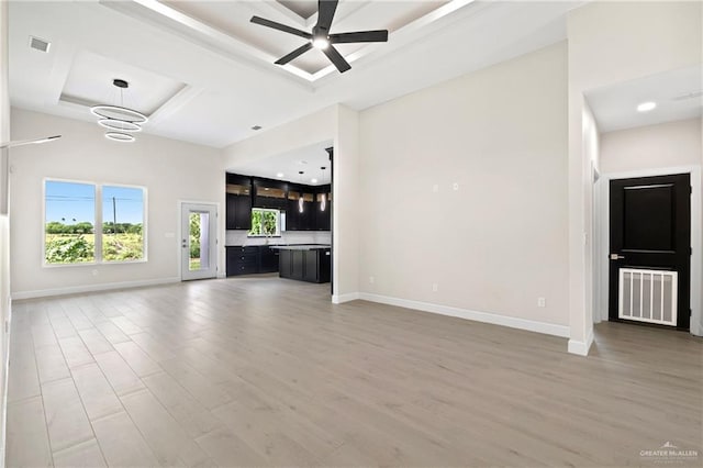 unfurnished living room featuring a tray ceiling, light wood-style flooring, and visible vents