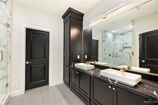 full bath with a sink, double vanity, a marble finish shower, and wood finished floors