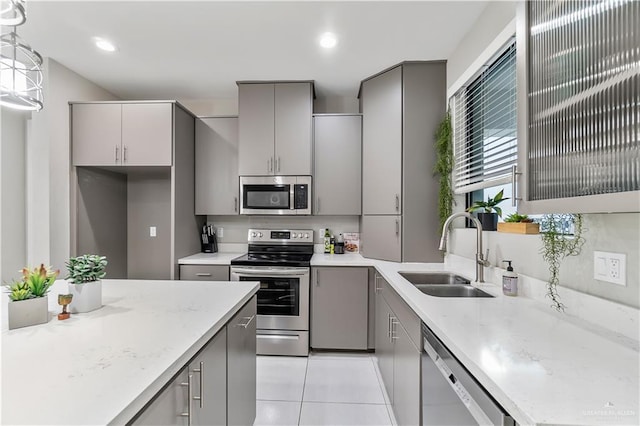 kitchen with appliances with stainless steel finishes, sink, light tile patterned floors, gray cabinets, and hanging light fixtures