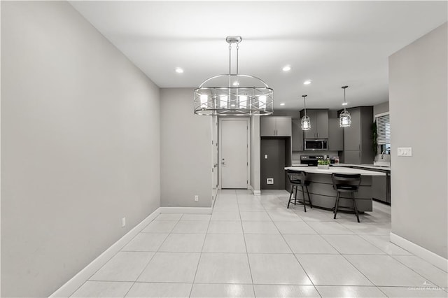 kitchen featuring appliances with stainless steel finishes, a kitchen breakfast bar, gray cabinetry, light tile patterned floors, and decorative light fixtures