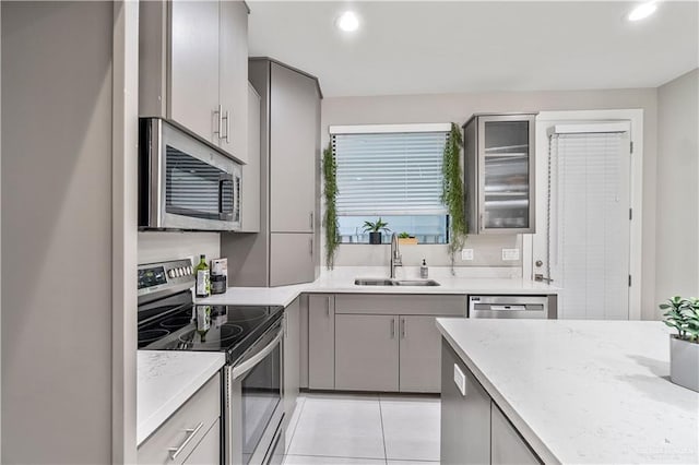 kitchen featuring gray cabinetry, sink, light tile patterned floors, appliances with stainless steel finishes, and light stone counters