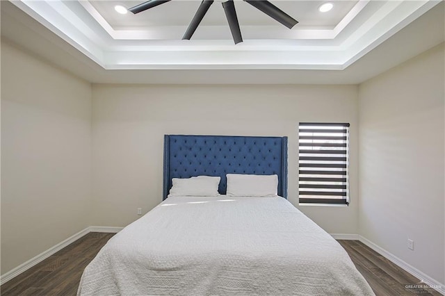 bedroom with ceiling fan, a tray ceiling, and dark hardwood / wood-style flooring