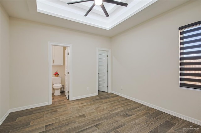 unfurnished bedroom with ceiling fan, ensuite bath, a tray ceiling, and dark hardwood / wood-style flooring